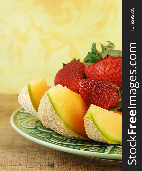 Sliced Cantaloupe and strawberries on a wooden table with a yellow background.