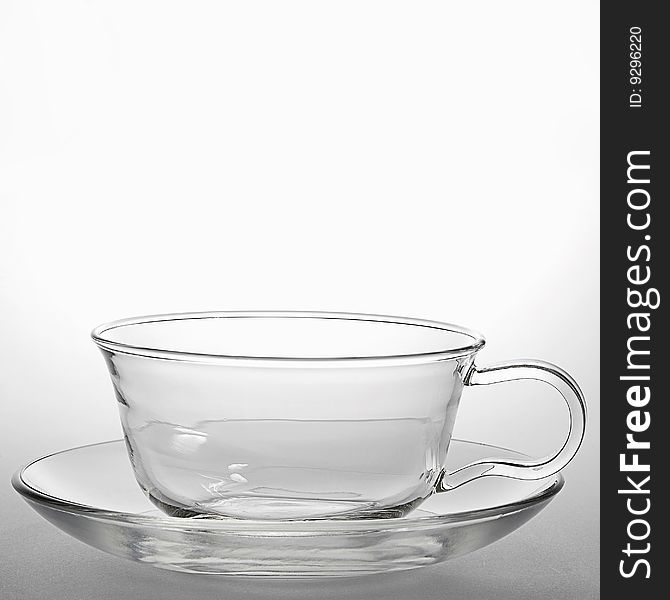 Glass teacup and a saucer on light background