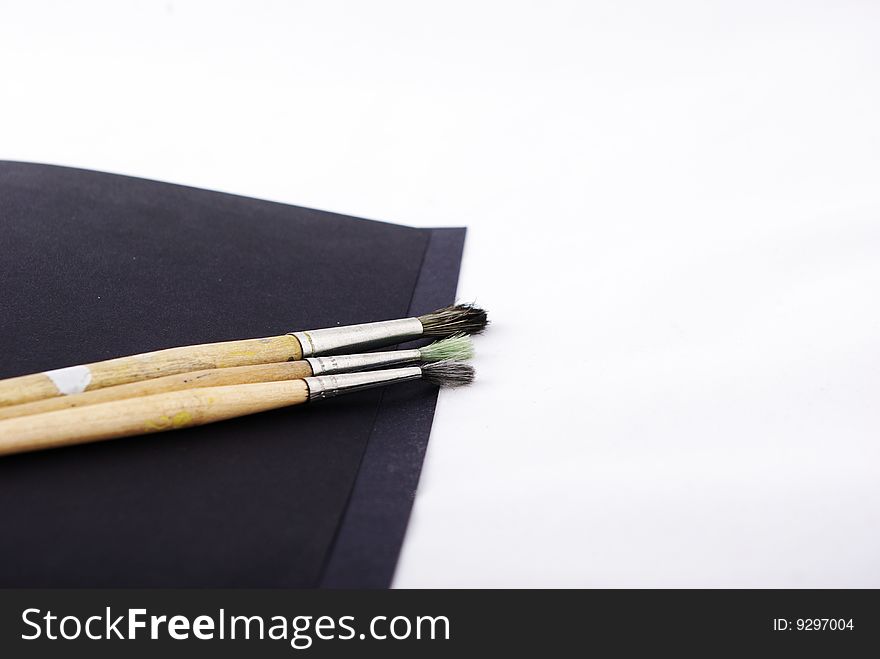 three paint brushes and black paper on white background.