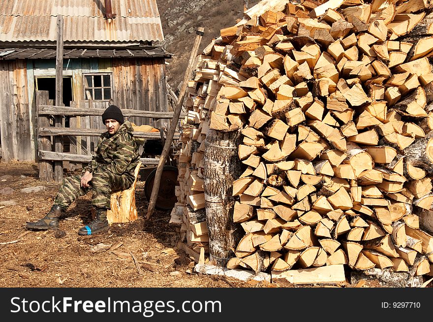 A man sitting near pile of firewood. A man sitting near pile of firewood