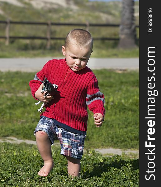 A young boy with scraped knee marches through deep grass and weeds while clutching favorite plastic toy animals
