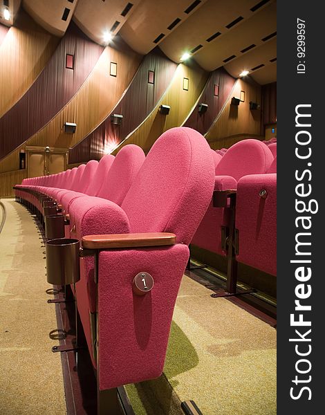 Pink row #1 of empty cinema auditorium with line of chairs.