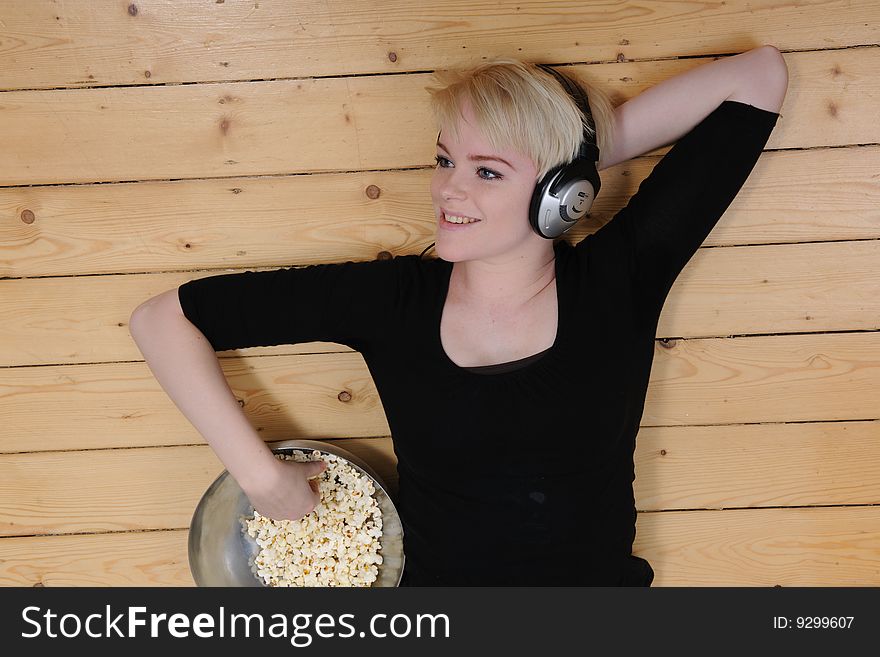 Girl lying on the  floor eating popcorn and listening to music. Girl lying on the  floor eating popcorn and listening to music