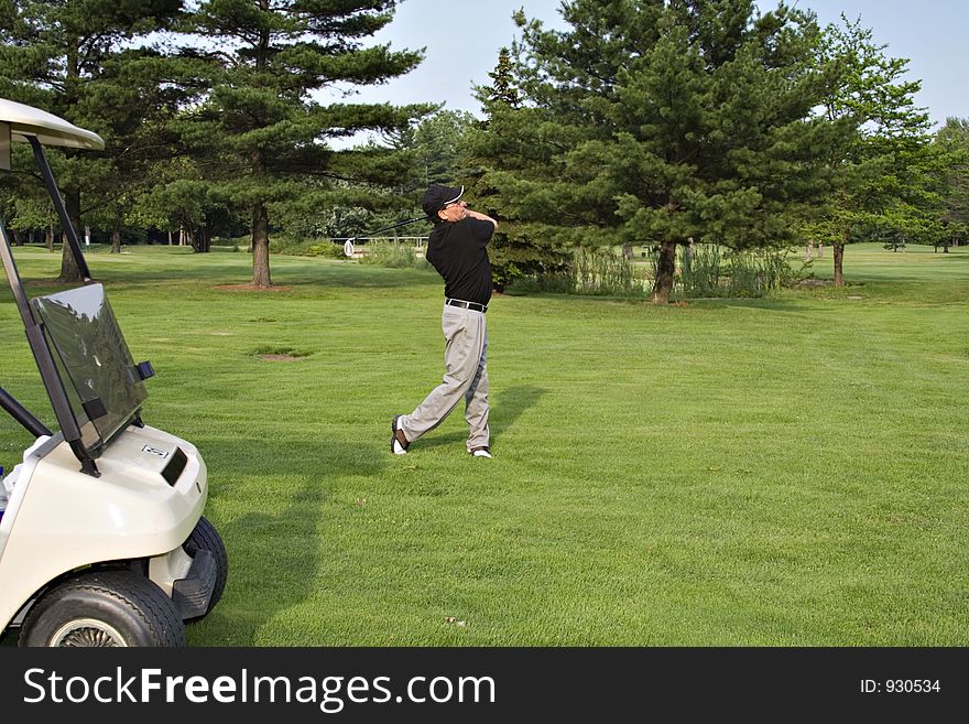 Man driving a ball from the fairway, golf cart in foreground.