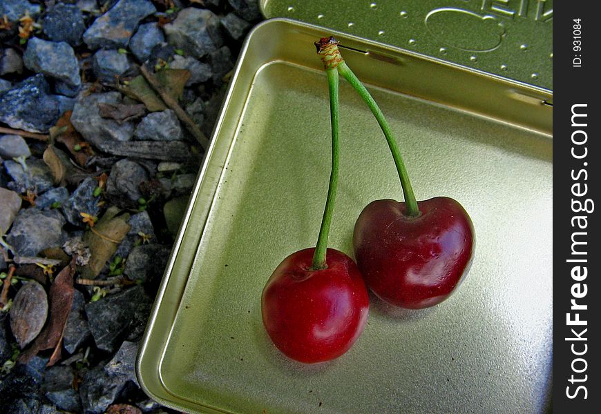 A couple of cherrys in a metal box over a rocky surface. A couple of cherrys in a metal box over a rocky surface.