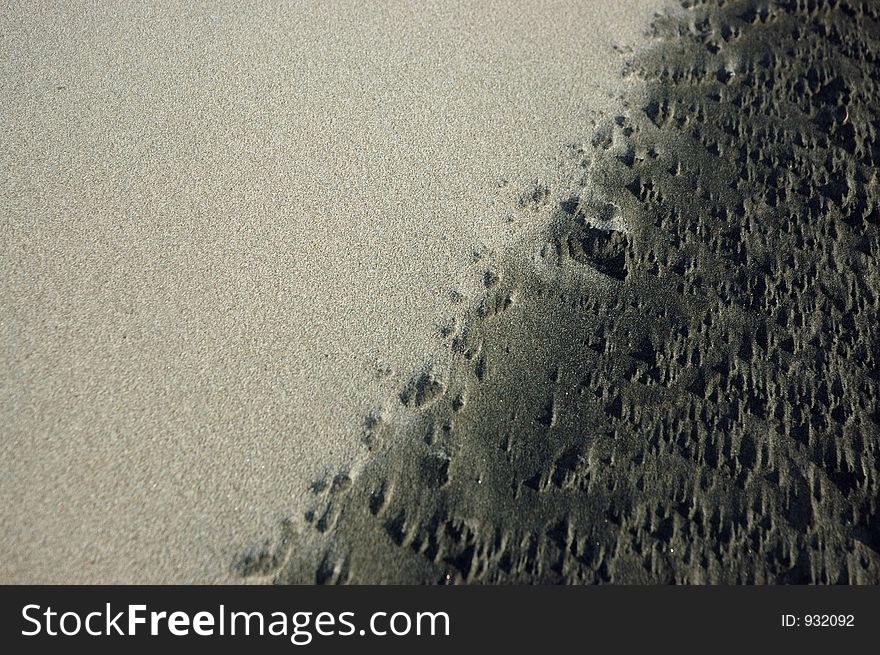 Lighter dry sand forms a layer over darker wet sand. Lighter dry sand forms a layer over darker wet sand