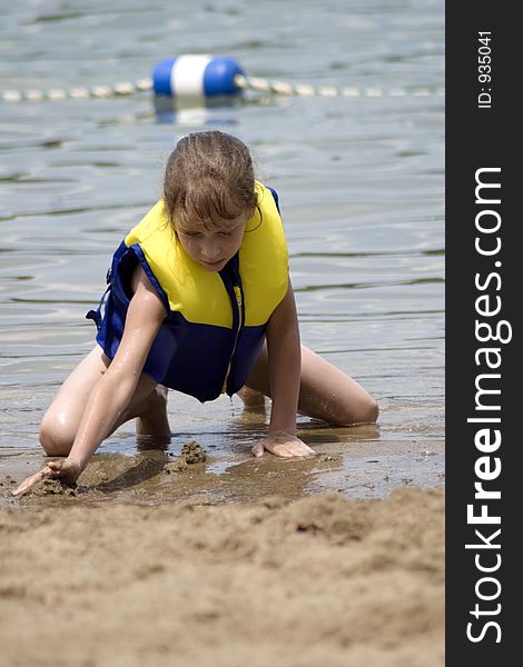 Young girl in lifejacket playing in the beach sand at the lake. Young girl in lifejacket playing in the beach sand at the lake.