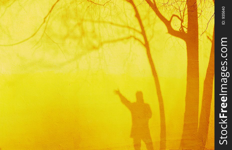 Shadow of a man waving and trees against a yellow wall in the evening sun