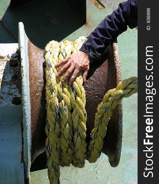 A rough sailor's hand, feeding rope back onto its housing, as the ship casts off. Great metaphor for the start of a voyage. A rough sailor's hand, feeding rope back onto its housing, as the ship casts off. Great metaphor for the start of a voyage.