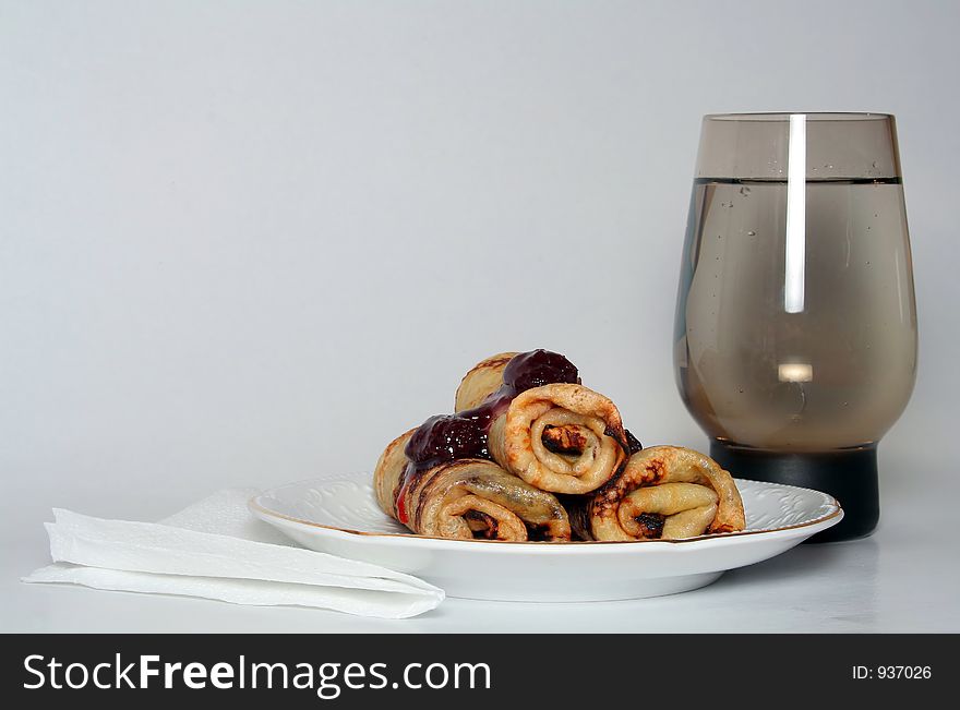 Rolled pancakes with sweet strawberry jam and glass of fresh mineral cool water. Rolled pancakes with sweet strawberry jam and glass of fresh mineral cool water