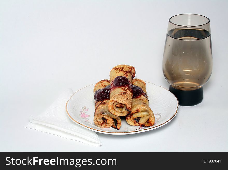 Rolled pancakes with sweet strawberry jam and glass of fresh mineral cool water. Rolled pancakes with sweet strawberry jam and glass of fresh mineral cool water