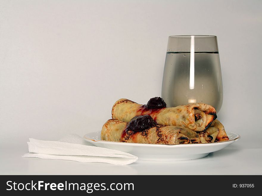 Rolled pancakes with sweet strawberry jam and glass of fresh mineral cool water. Rolled pancakes with sweet strawberry jam and glass of fresh mineral cool water