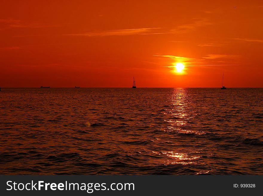 Beautiful sunset with clear orange sky and sailboats in the background