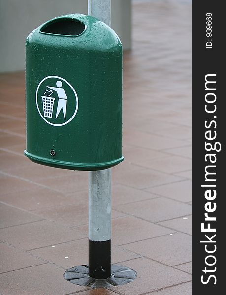 A green trash bin in a city. The Bin is fastened to a lightpole. A green trash bin in a city. The Bin is fastened to a lightpole.