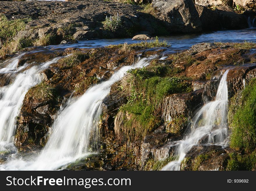 Photograph of small river, flowing, waterfalls, lush green vegetation and genuine tranquil athmosphere