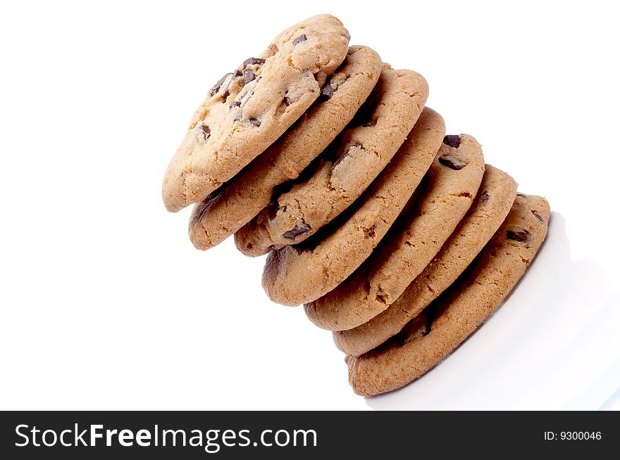 A tilted image of a stack of 7 chocolate chip cookies on a white reflective surface. A tilted image of a stack of 7 chocolate chip cookies on a white reflective surface