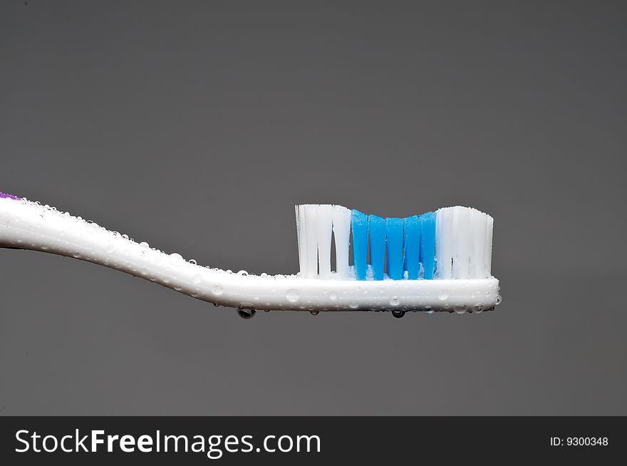 A horizontal closeup of a manual toothbrush with water droplets on a gray background