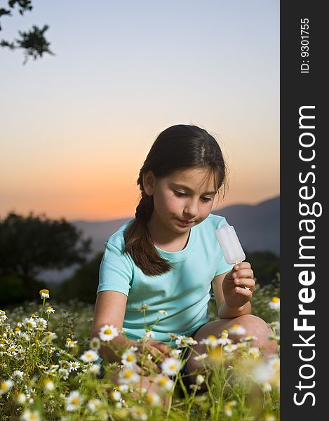 Young girl having a popsicle in a flower field at sunset