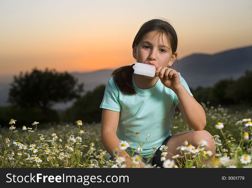 Young girl having a Popsicle in a flower field at sunset