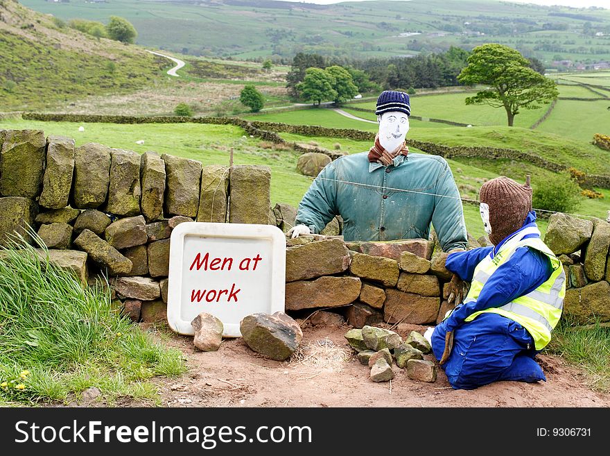 The photo shows scarecrow type representations of men building a wall. The photo shows scarecrow type representations of men building a wall