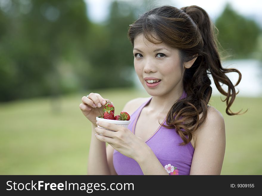 An asian lady is taking a break enjoying a bowl of healthly strawberry snacks. An asian lady is taking a break enjoying a bowl of healthly strawberry snacks.