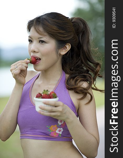 An asian lady is taking a break enjoying a bowl of healthly strawberry snacks. An asian lady is taking a break enjoying a bowl of healthly strawberry snacks.