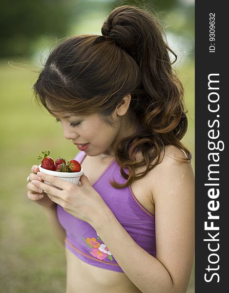 An asian lady taking a break enjoying a bowl of healthy strawberries.  She is enjoying the aroma from the bowl. An asian lady taking a break enjoying a bowl of healthy strawberries.  She is enjoying the aroma from the bowl.