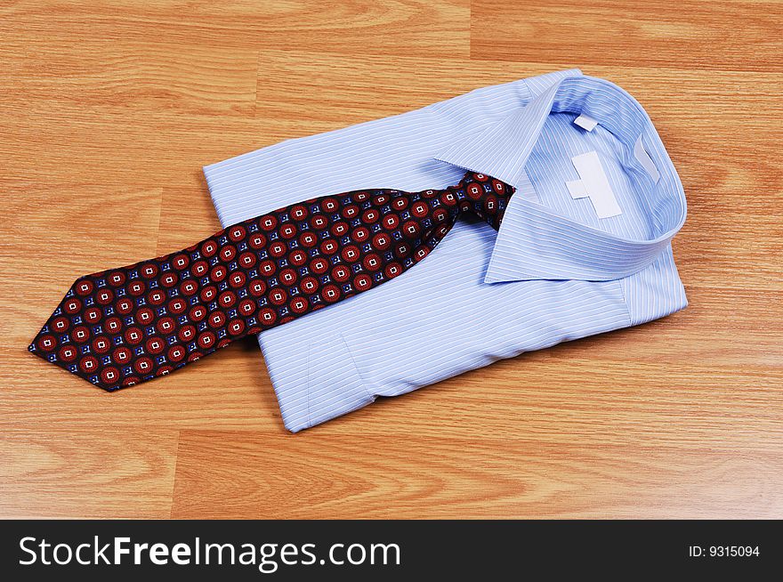 A light blue dress shirt on a wood surface with an red and black tie for sale in the store. A light blue dress shirt on a wood surface with an red and black tie for sale in the store.