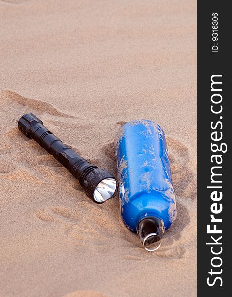 Sport bottle and flashlight in desert