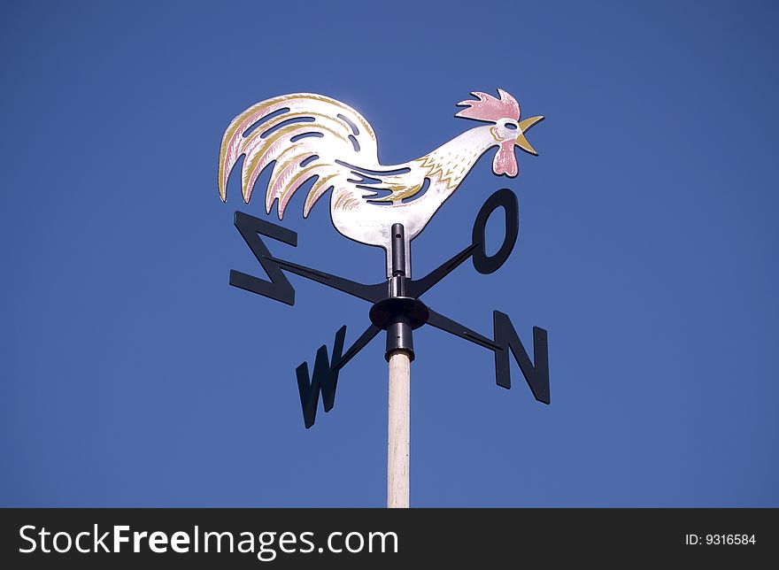 Weather vane - cockerel which reflected sun against bright-dark blue sky. Weather vane - cockerel which reflected sun against bright-dark blue sky