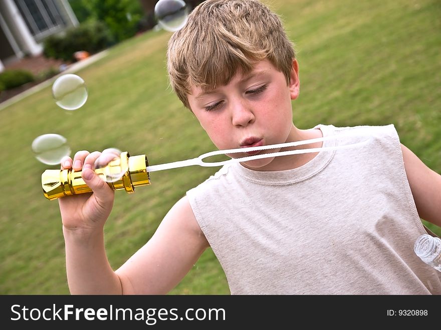 A boy in the yard blowing bubbles. Having fun at home; wind and green energy; concept or metaphor. A boy in the yard blowing bubbles. Having fun at home; wind and green energy; concept or metaphor.