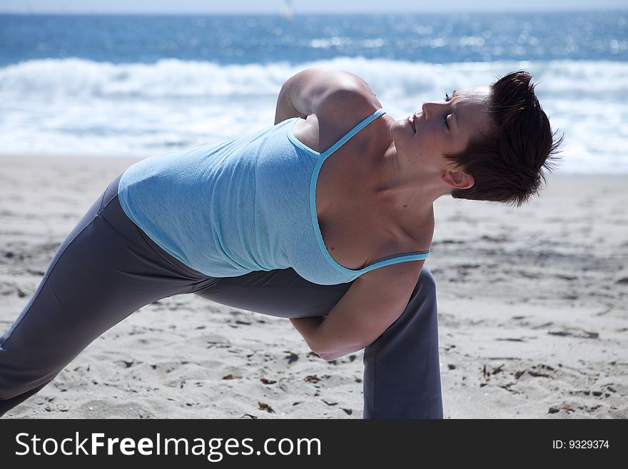 An attractive woman practicing yoga at the beach with a blue shirt. An attractive woman practicing yoga at the beach with a blue shirt