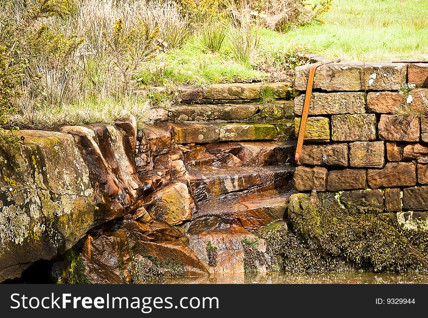 View of Brodick old harbour showing steps cut in to the sand stone slope in to the sea