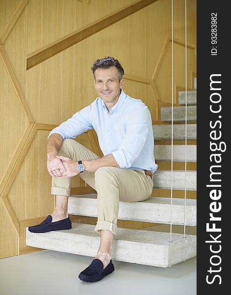 Full length shot of a smiling casual man sitting on stairs at home and enjoy life. Full length shot of a smiling casual man sitting on stairs at home and enjoy life.