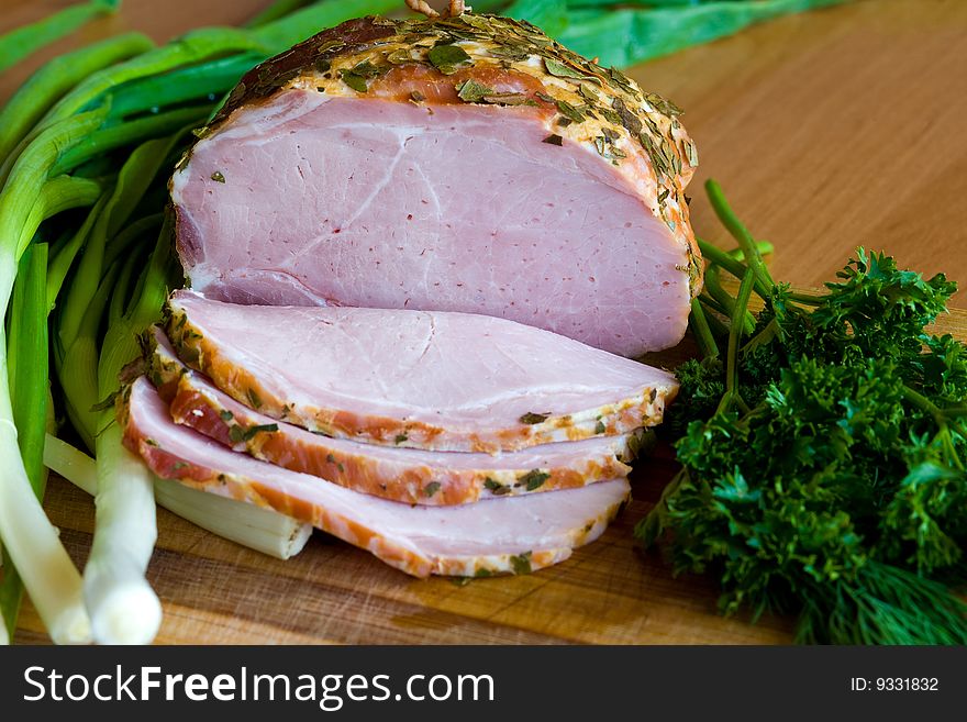 Appetizing slices of ham with potherbs on the kitchen table. Appetizing slices of ham with potherbs on the kitchen table