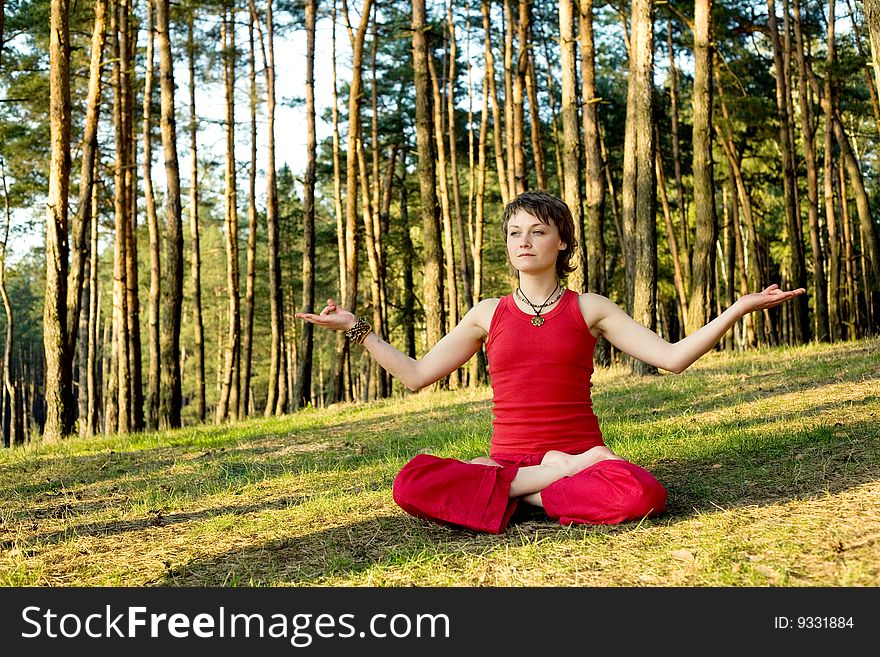A young pretty woman sitting in lotos pose on the forest background