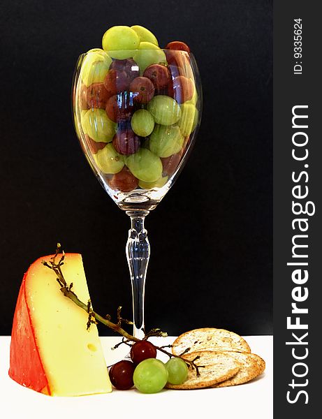 Wine glass filled with grapes, surrounded by cheese and crackers. Wine glass filled with grapes, surrounded by cheese and crackers