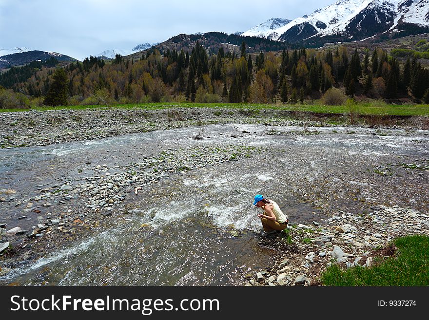 The girl drinks water from the mountain river