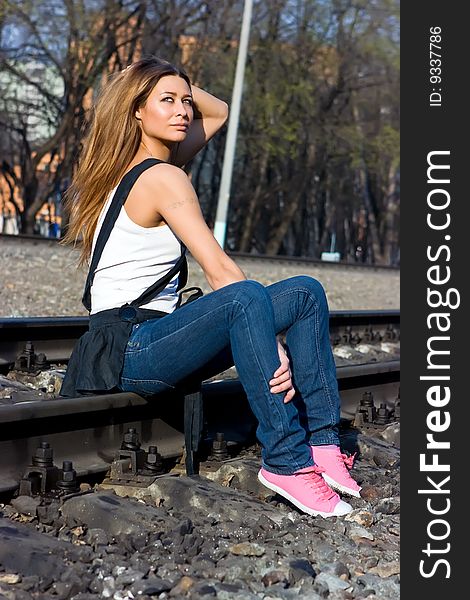 Brunette model sitting on railroad in her jeans and pink gymshoes. Brunette model sitting on railroad in her jeans and pink gymshoes