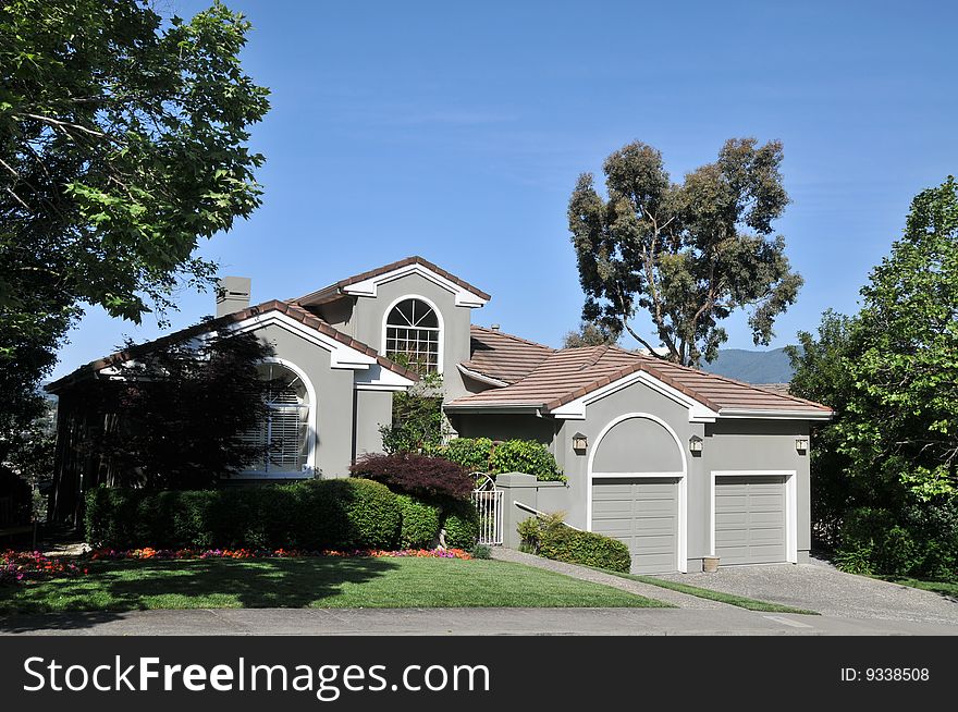 House surrounded by trees and blue sky. Split level with grass yard and shrubs.