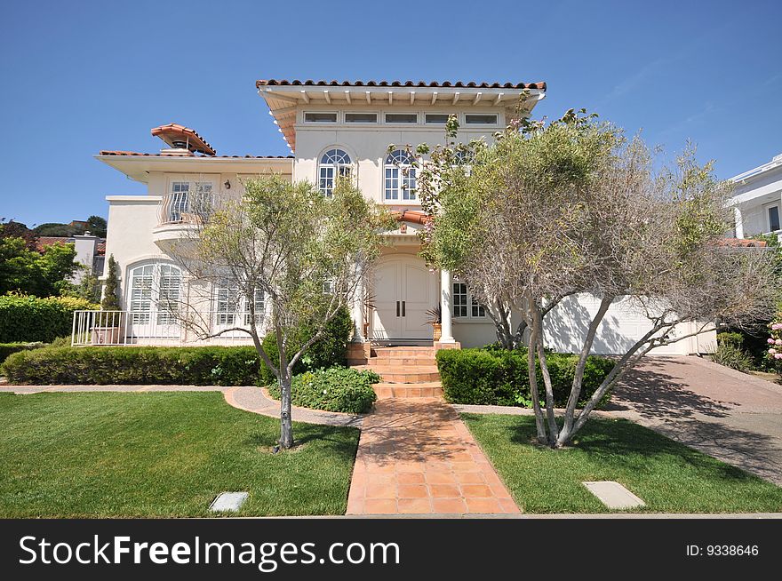 House with trees on each side of the walkway to the front double doors. Blue sky. Two levels with grass yard, trees and shrubs. House with trees on each side of the walkway to the front double doors. Blue sky. Two levels with grass yard, trees and shrubs.