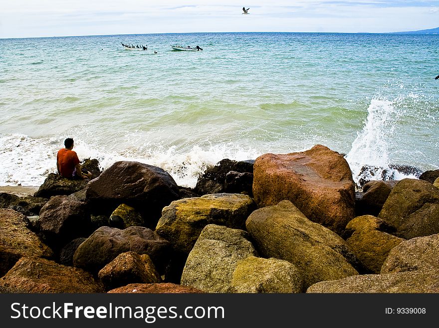 Man sitting on rocks, watching the sea