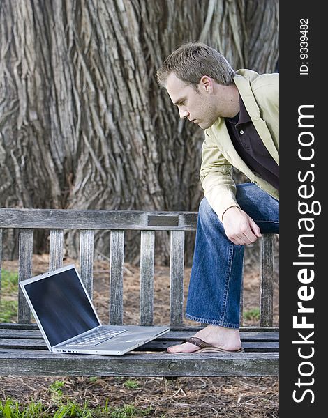 Young man studying a laptop computer on a park bench. Young man studying a laptop computer on a park bench