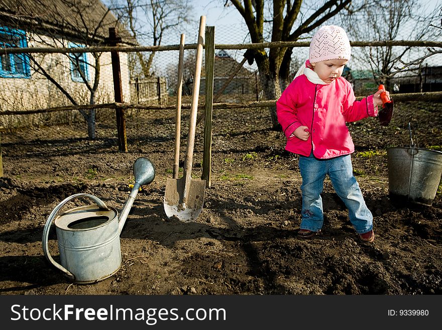 A pretty little girl  in  her grandfather's  kitchen garden  with  a toy  spade in  a hand. A pretty little girl  in  her grandfather's  kitchen garden  with  a toy  spade in  a hand