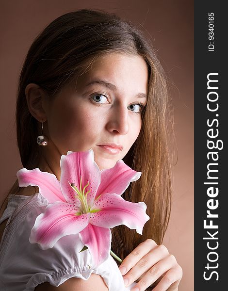 A pretty young woman with long brown hair posing with a pink lily in her hand. A pretty young woman with long brown hair posing with a pink lily in her hand