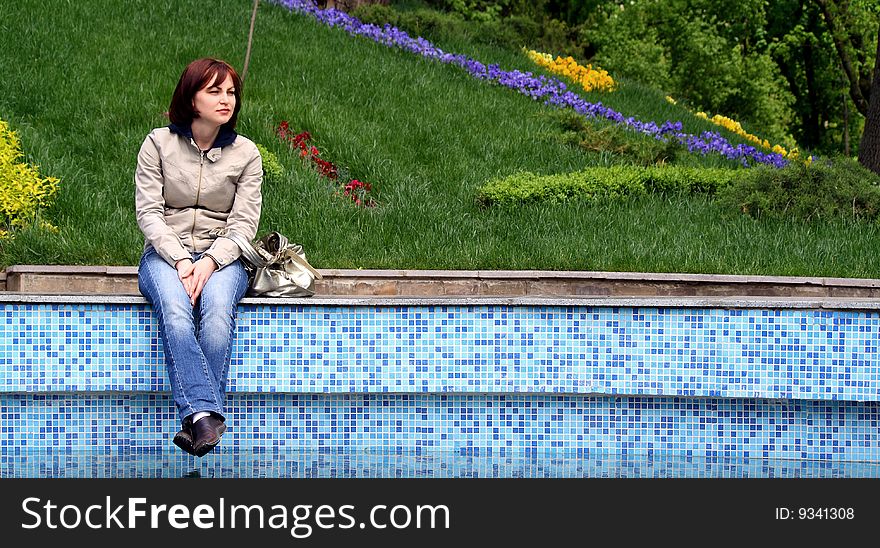 The girl near the pool, sat down to have a rest and look at floating birds. The girl near the pool, sat down to have a rest and look at floating birds