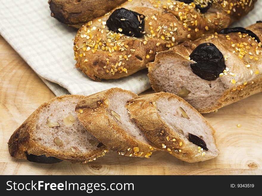 Close up on three baguettes with prunes and corn grain on a wood board, one sliced. Close up on three baguettes with prunes and corn grain on a wood board, one sliced