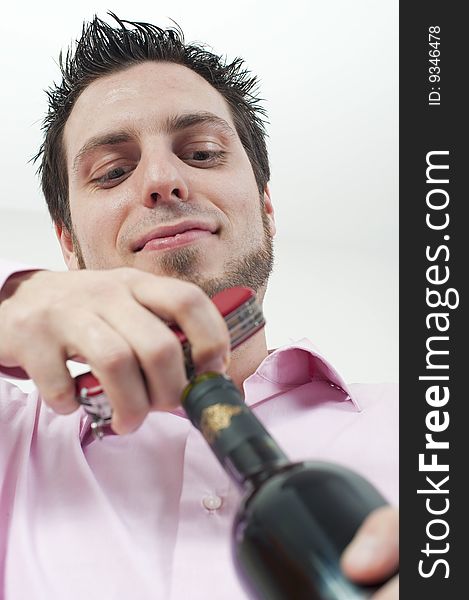 Young man, opening a bottle of red wine with cork screw, looking satisfied. Young man, opening a bottle of red wine with cork screw, looking satisfied