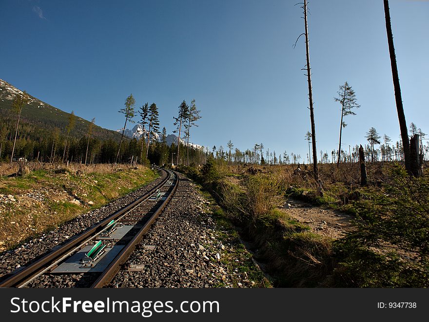 Cable railway track in mountains with grass and trees and blue sky