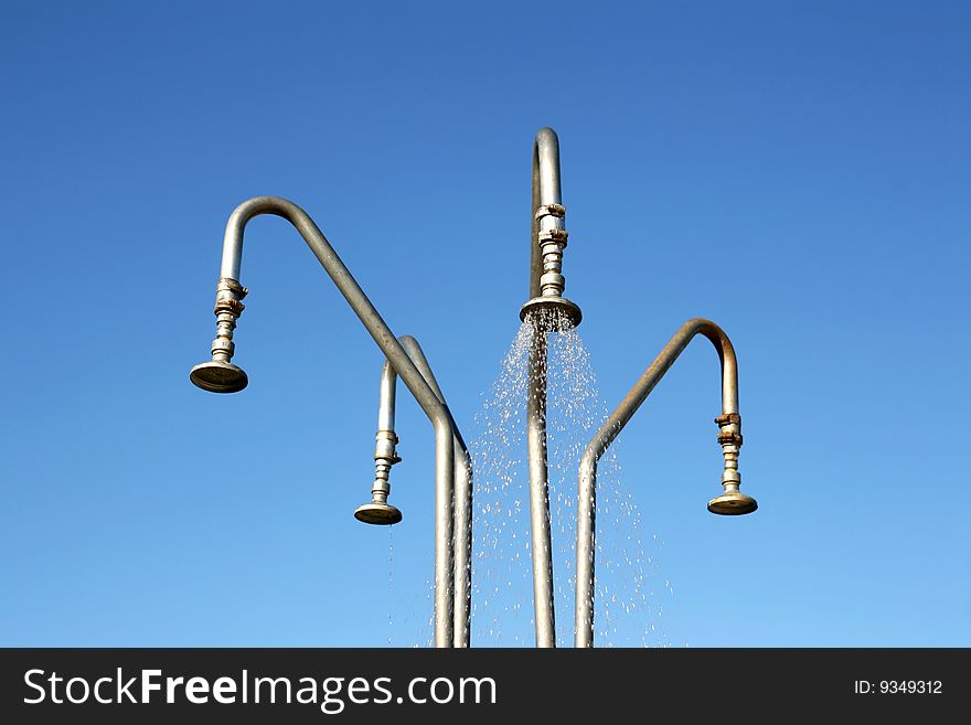 Four outdoor shower heads over deep blue and cloudless sky. Water leaking from one shower head. Green environment concept.
